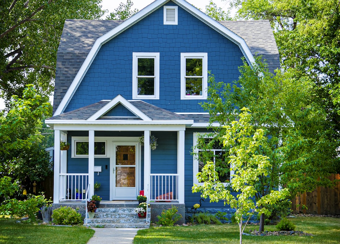 A blue colonial home with a front porch on a residential street