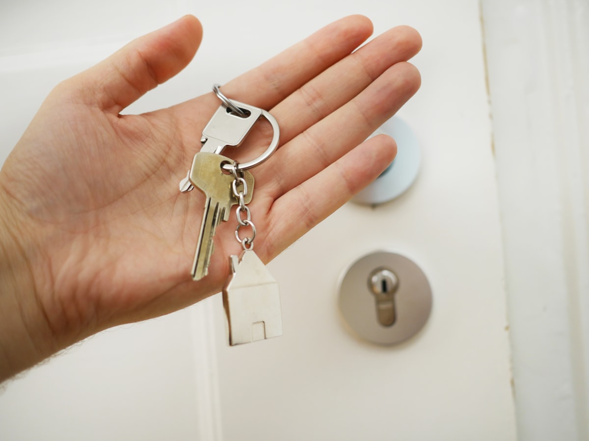 A set of house keys with a house keyring, held in an open hand
